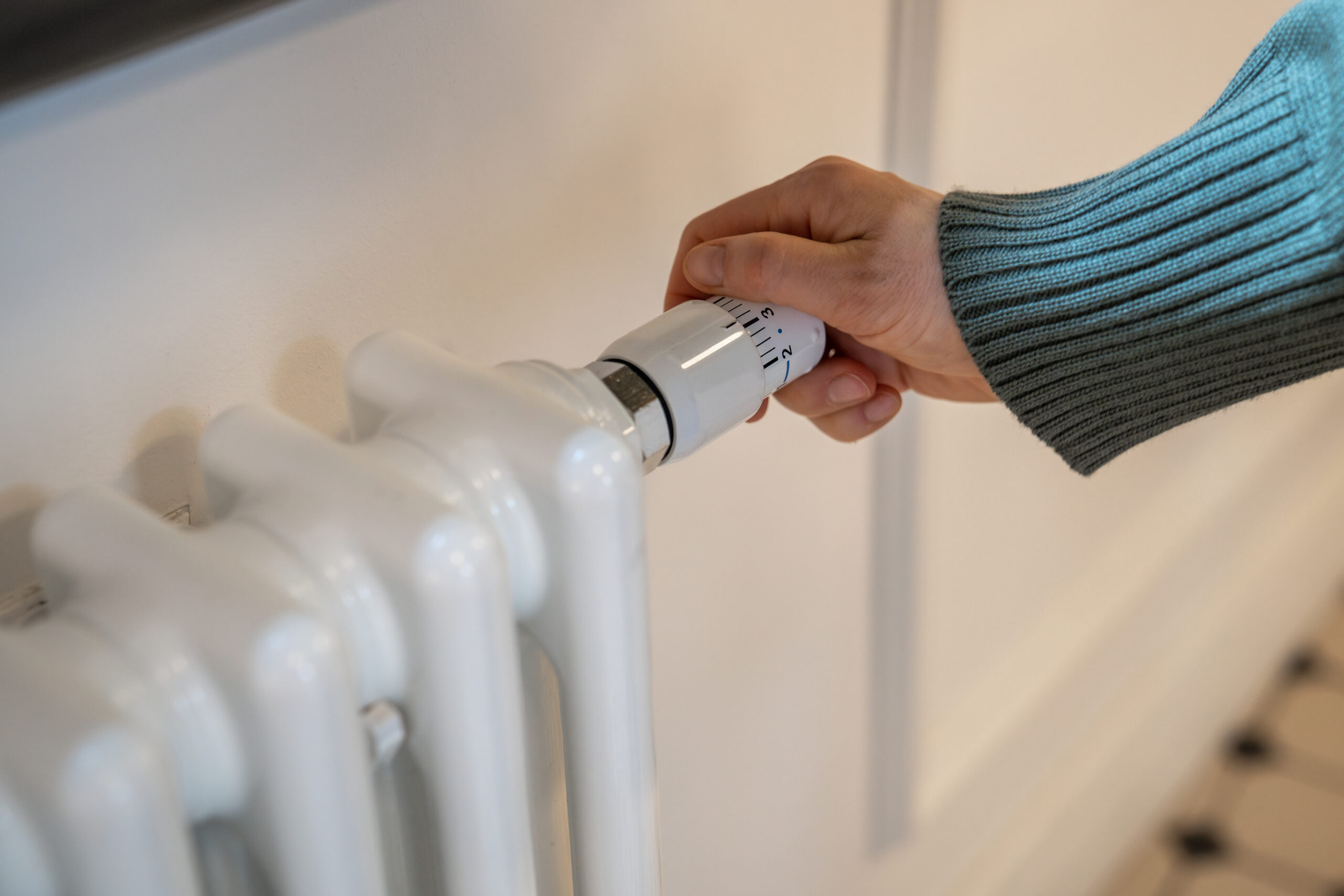Hand adjusting heater knob, regulating temperature at home in winter during heating season. Radiator equipped with thermostat allowing to save, economize energy, limit temperature in apartment